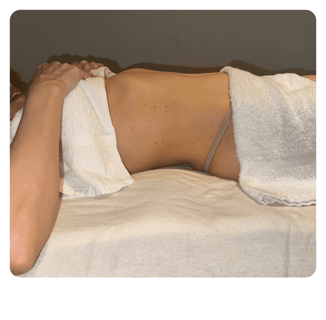 A woman laying on top of a bed with white sheets.